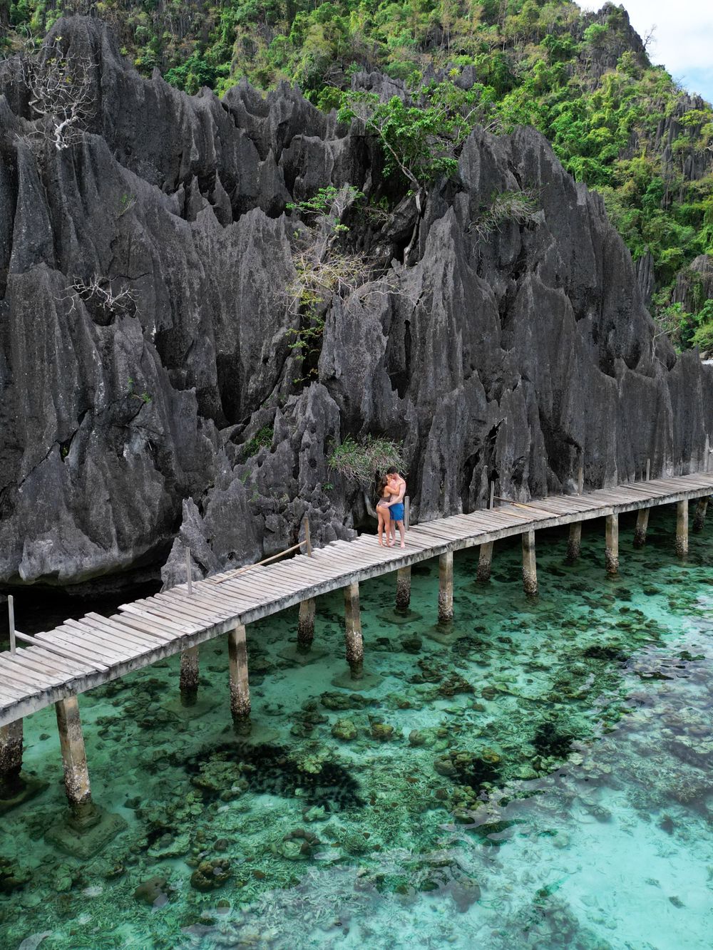 Wooden walkway over crystal clear turquoise waters next to dramatic limestone cliffs.