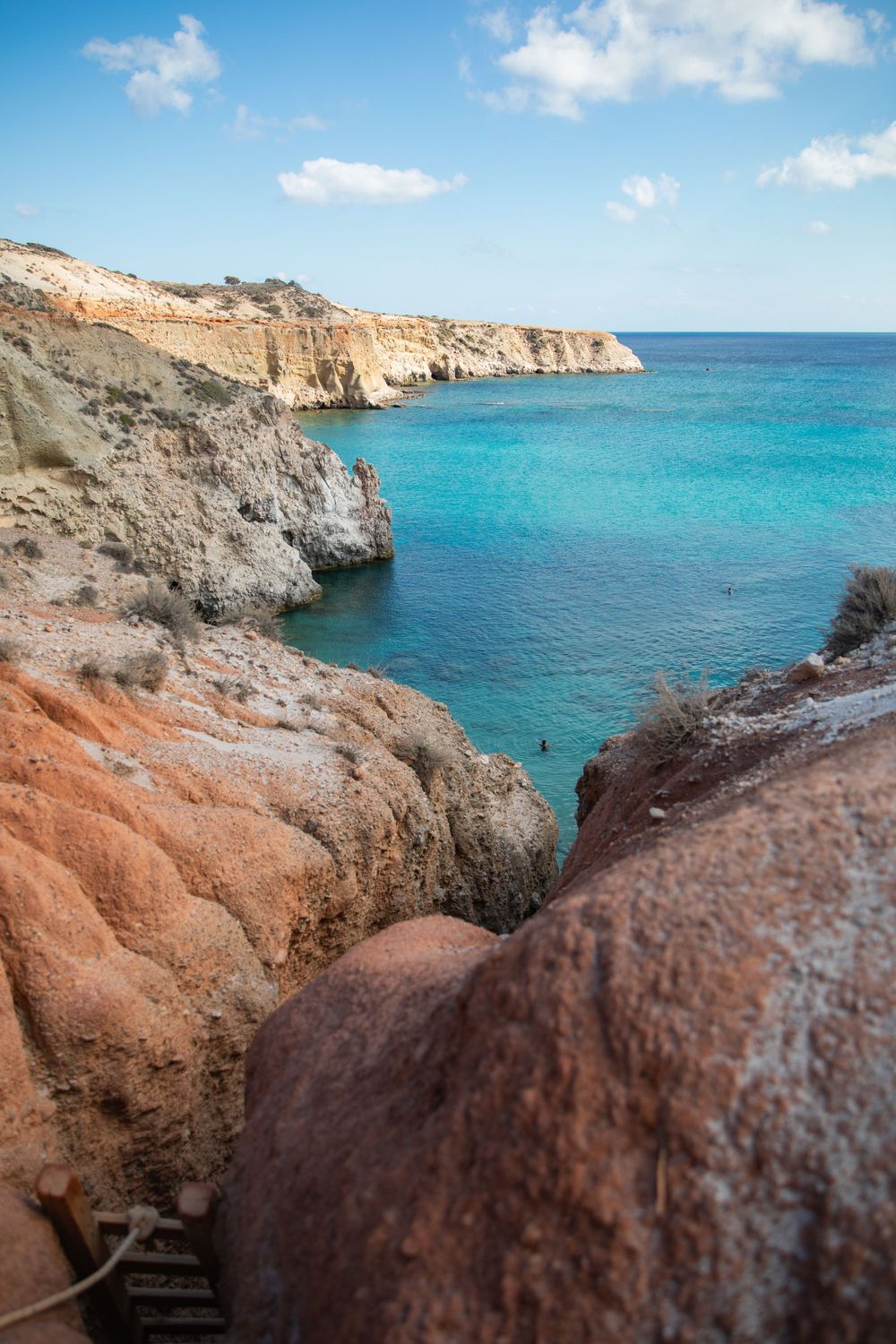 Turquoise Mediterranean waters meet rugged red cliffs along a dramatic coastal landscape.