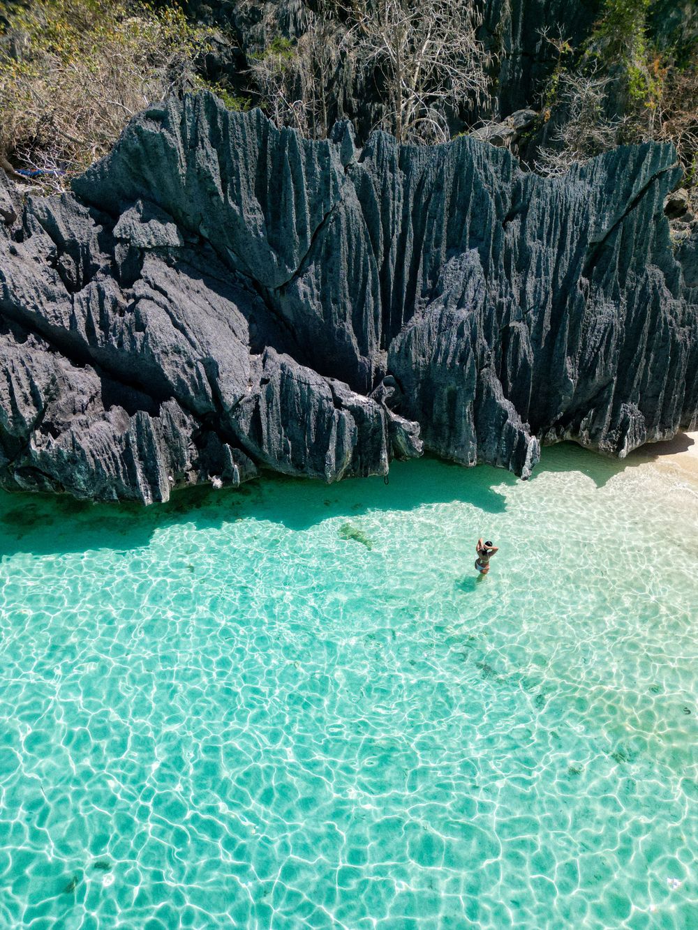 Crystal clear turquoise water meets dramatic limestone cliffs in a secluded tropical cove.