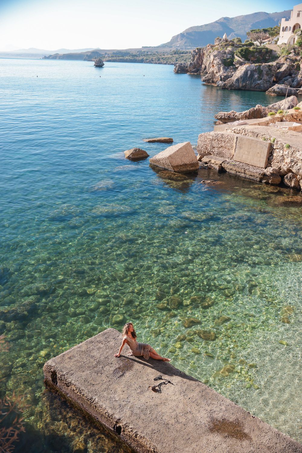 Crystal clear Mediterranean waters meet rocky coastline with scenic concrete platform.