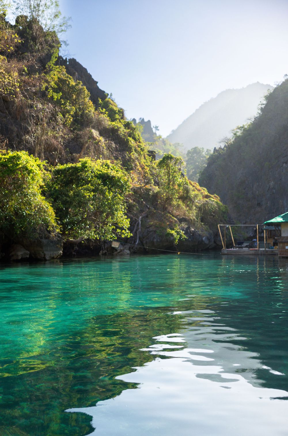 Tranquil turquoise lagoon water surrounded by limestone cliffs and lush vegetation in Palawan, Philippines.