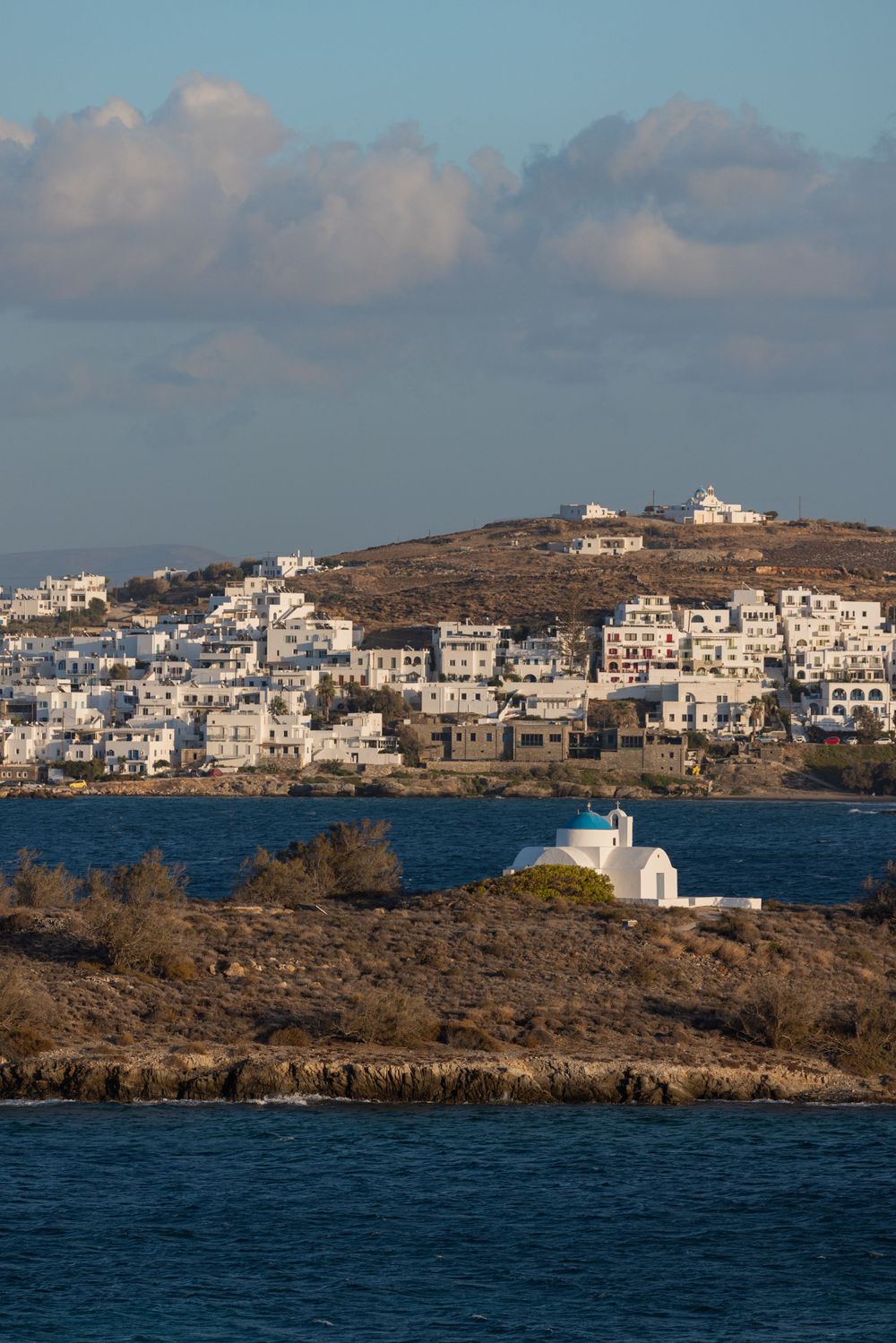 Traditional white Greek island village perched on hillside overlooking blue Mediterranean Sea.