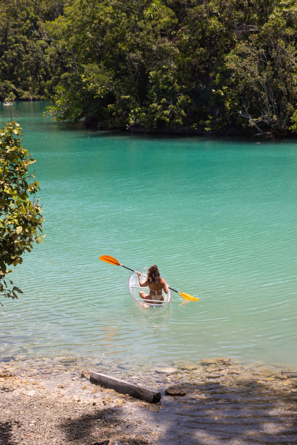 Peaceful turquoise lake scene with kayaker paddling through crystal clear waters surrounded by forest.
