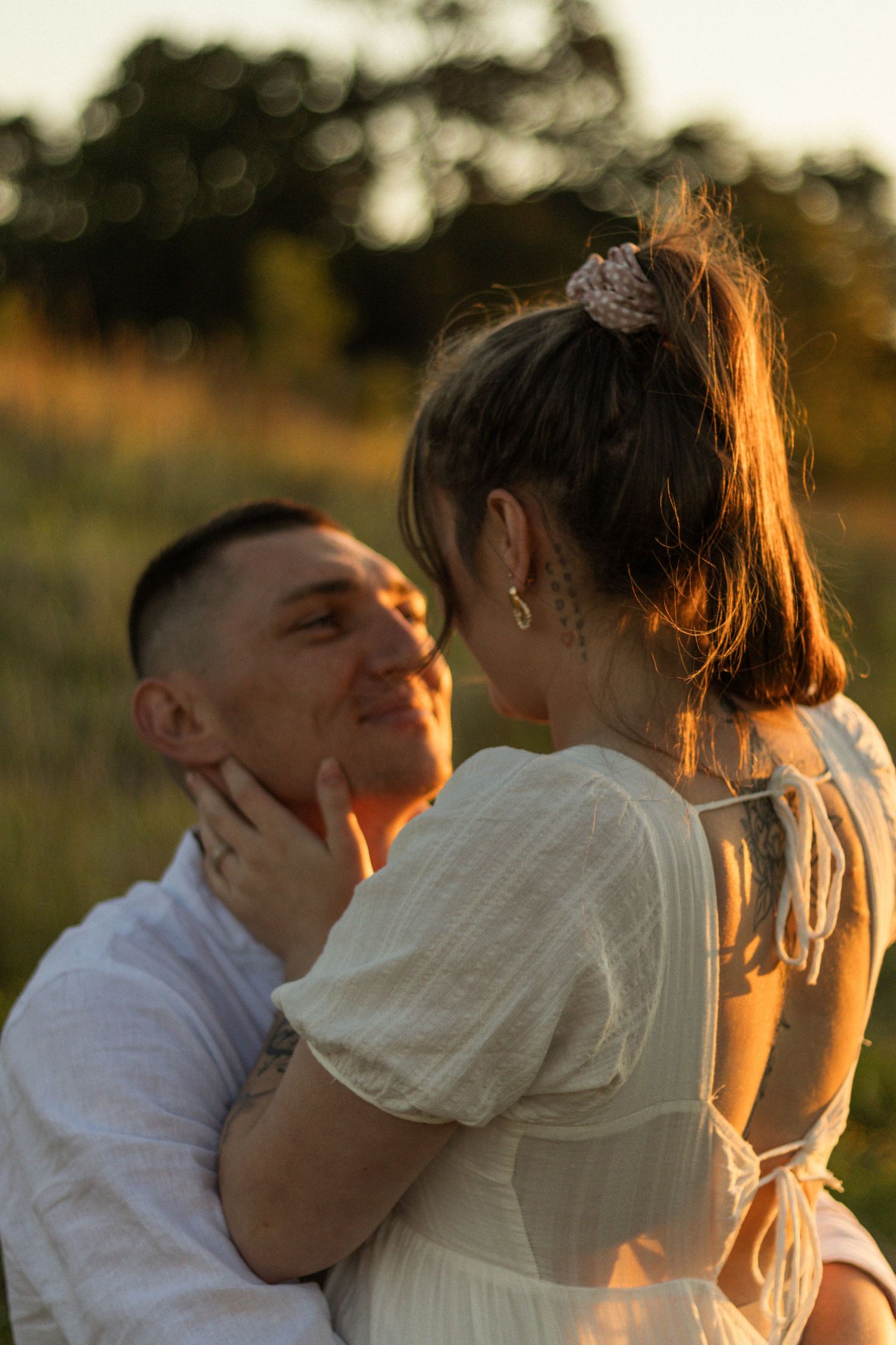 Romantic couple sharing an intimate moment in golden sunset light while wearing white clothing in a natural outdoor setting.
