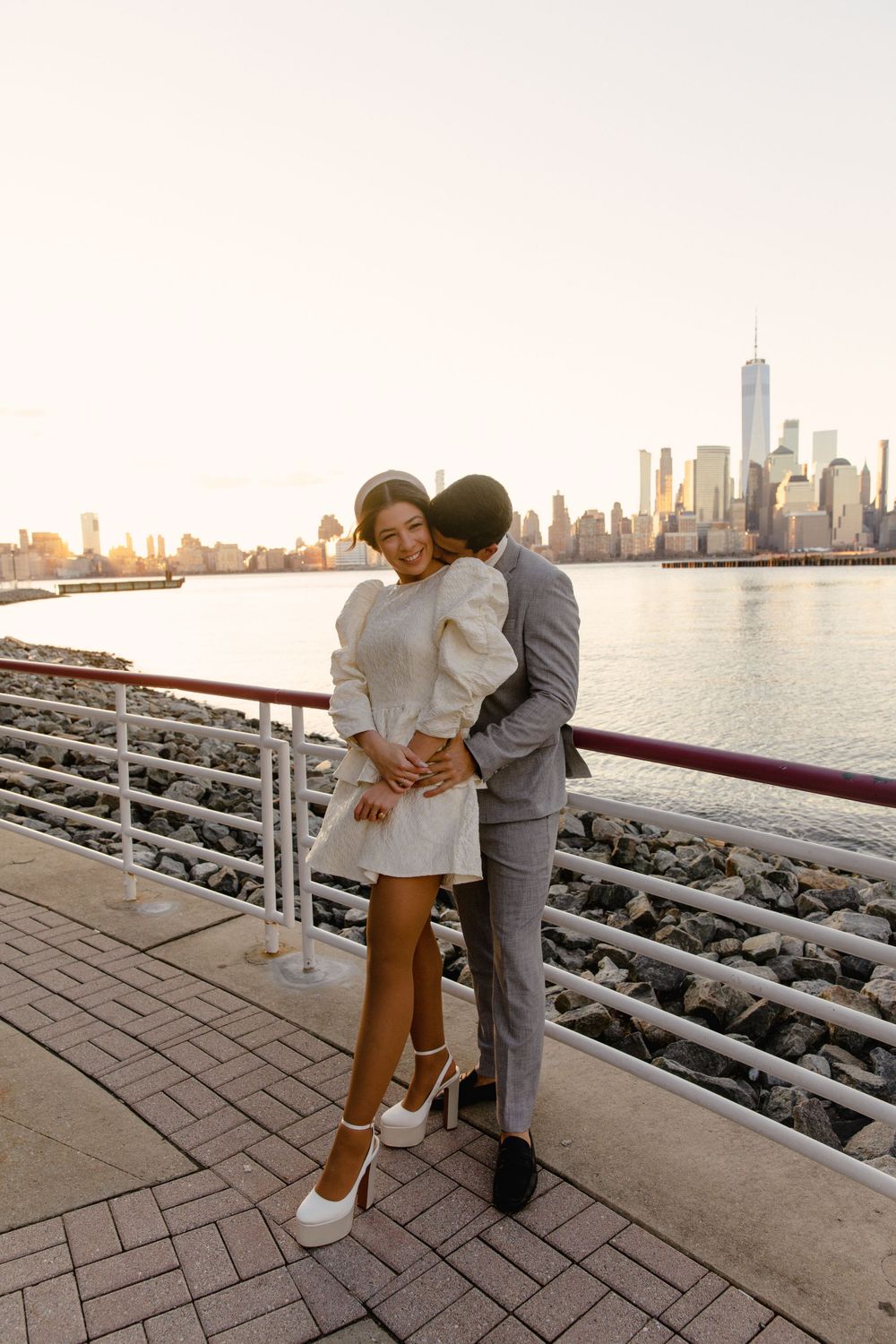 Sunset engagement photo of couple in formal attire with New York City skyline.
