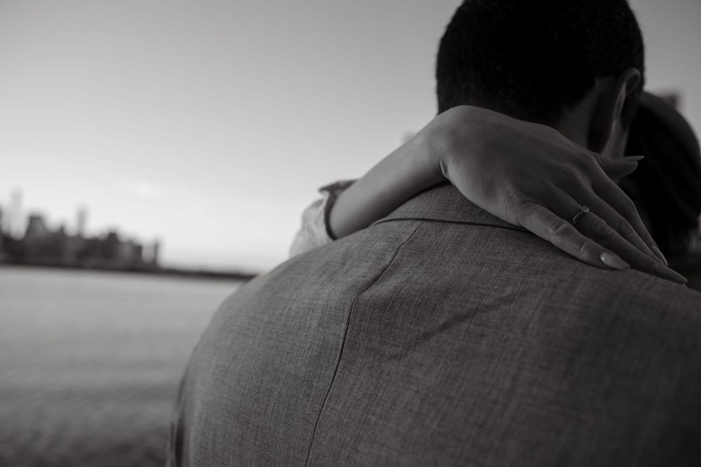 Black and white photo capturing embrace with urban skyline in background.