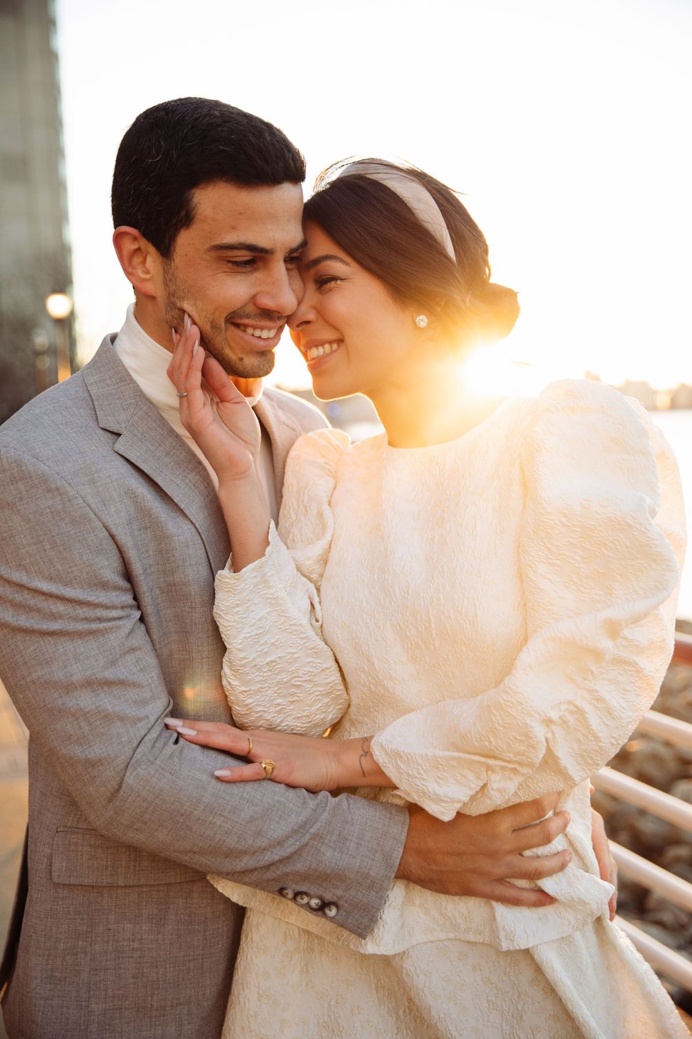 Golden hour portrait of couple in formal wear sharing joyful moment by waterfront.