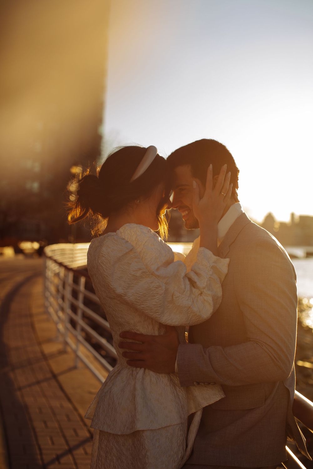Silhouetted couple sharing romantic moment at golden hour by waterfront railing.