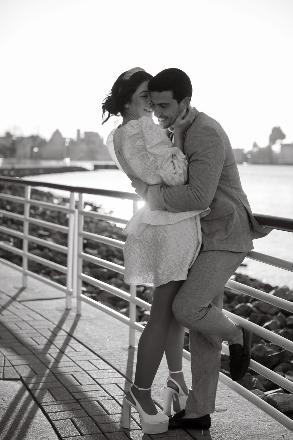 Black and white photo of romantic couple embracing on waterfront boardwalk.