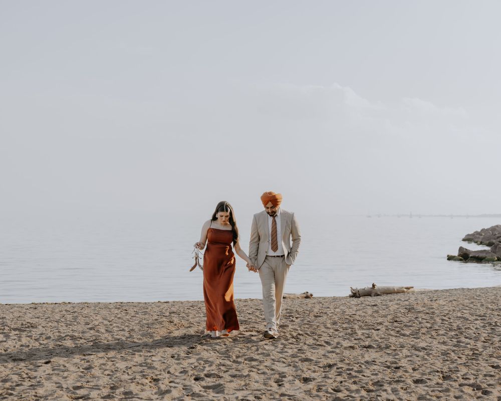 A couple walks together on a misty beach, with the person in rust-colored dress and other in light gray suit.