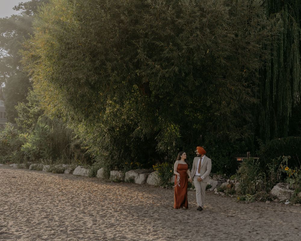 A couple strolls along a stone-lined path near lush greenery and trees.