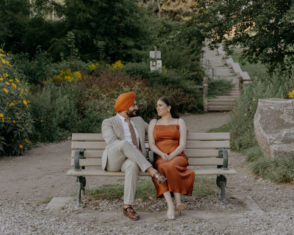 A couple shares an intimate conversation while sitting on a park bench surrounded by flowers.