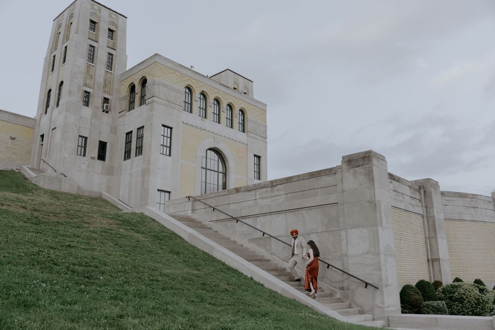 A couple climbs stairs of a majestic white building with tower and arched windows.
