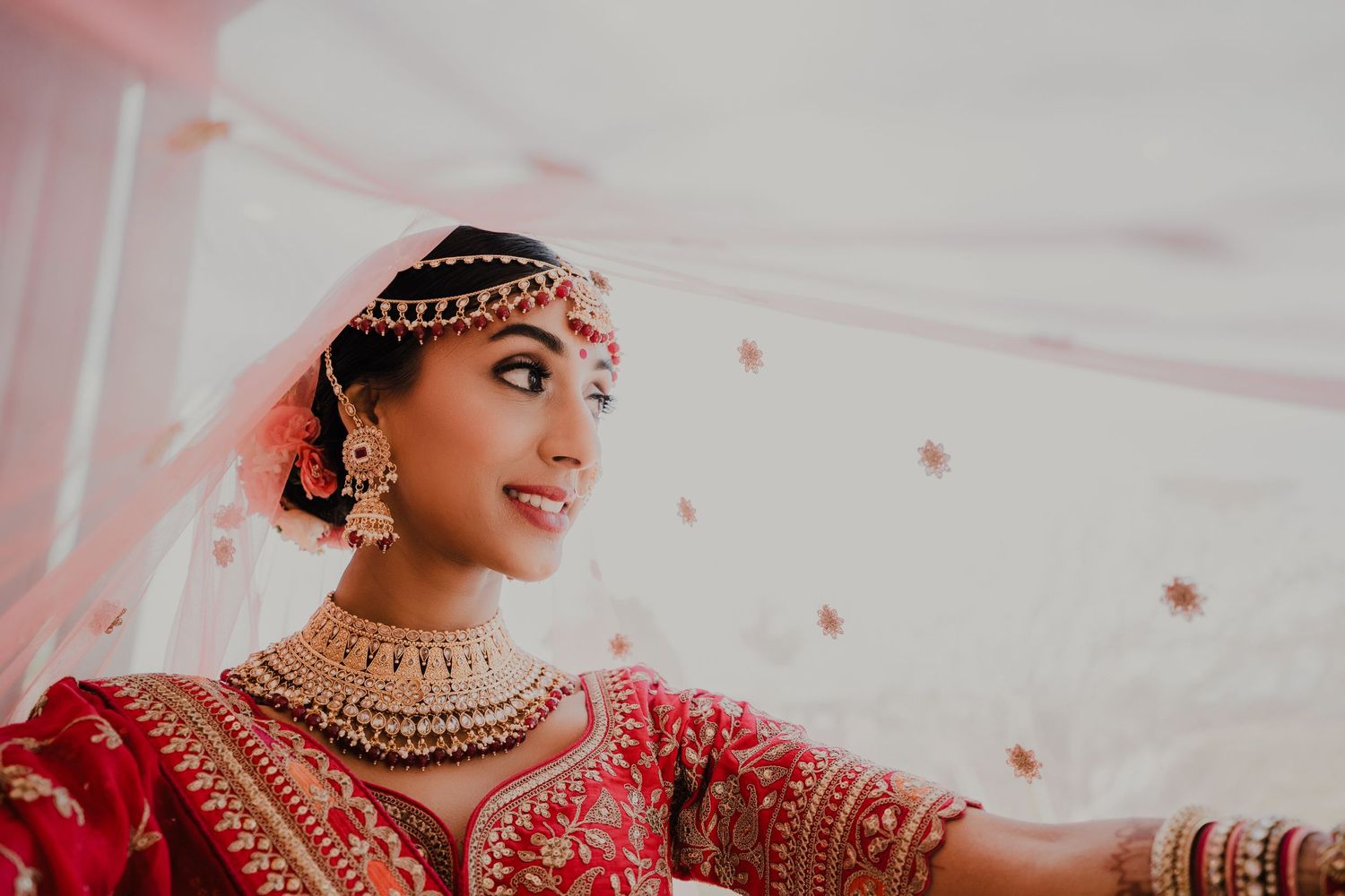 South Asian bride in red traditional attire with ornate jewelry and headpiece.