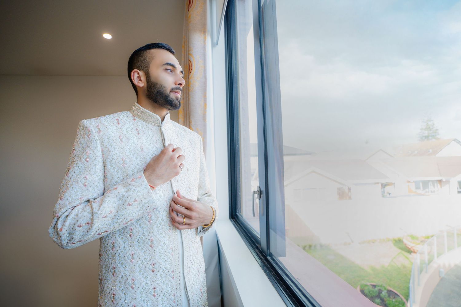 Person in white formal attire standing by window in contemplative pose.