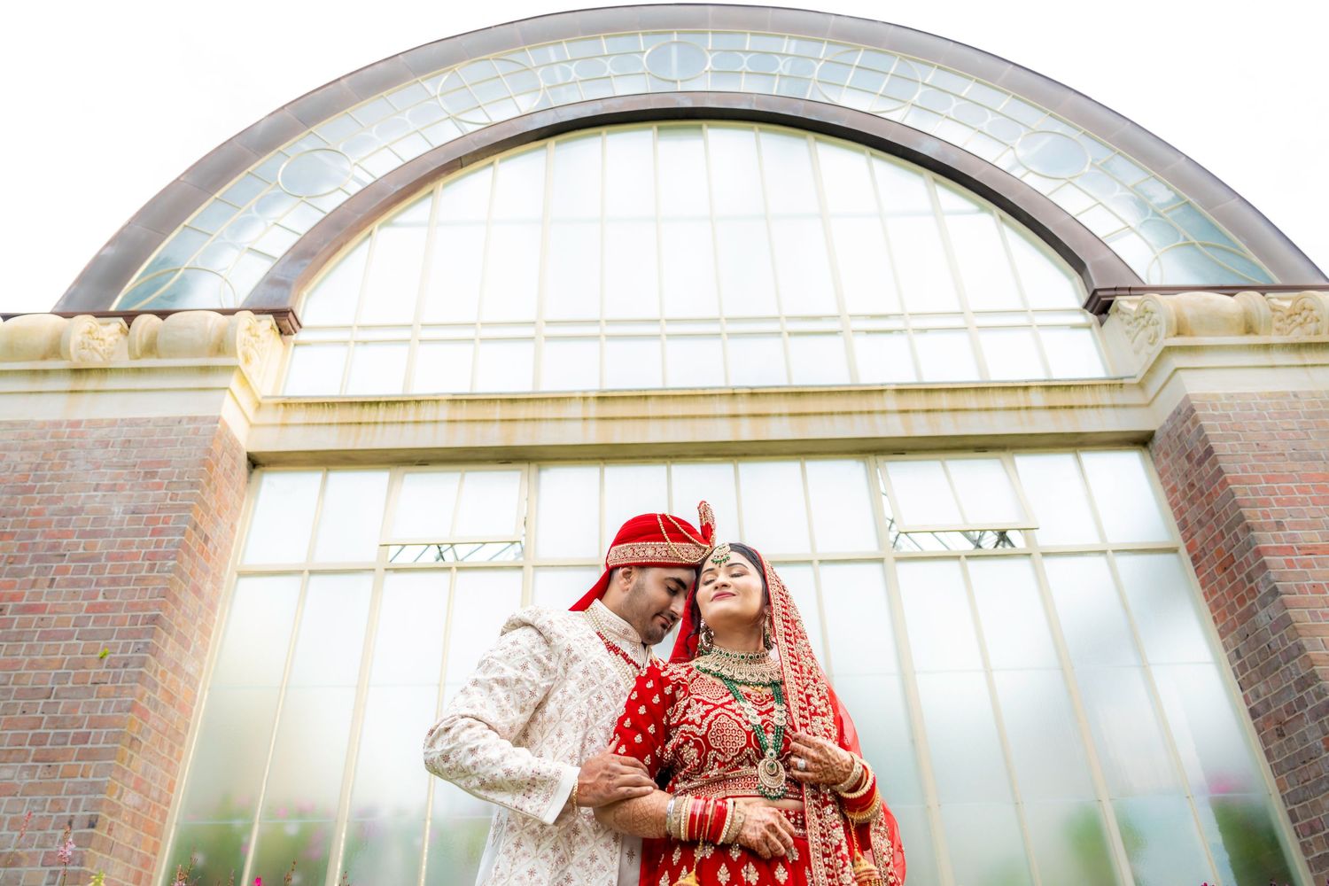 Traditional South Asian wedding couple posing under an arched architectural feature.