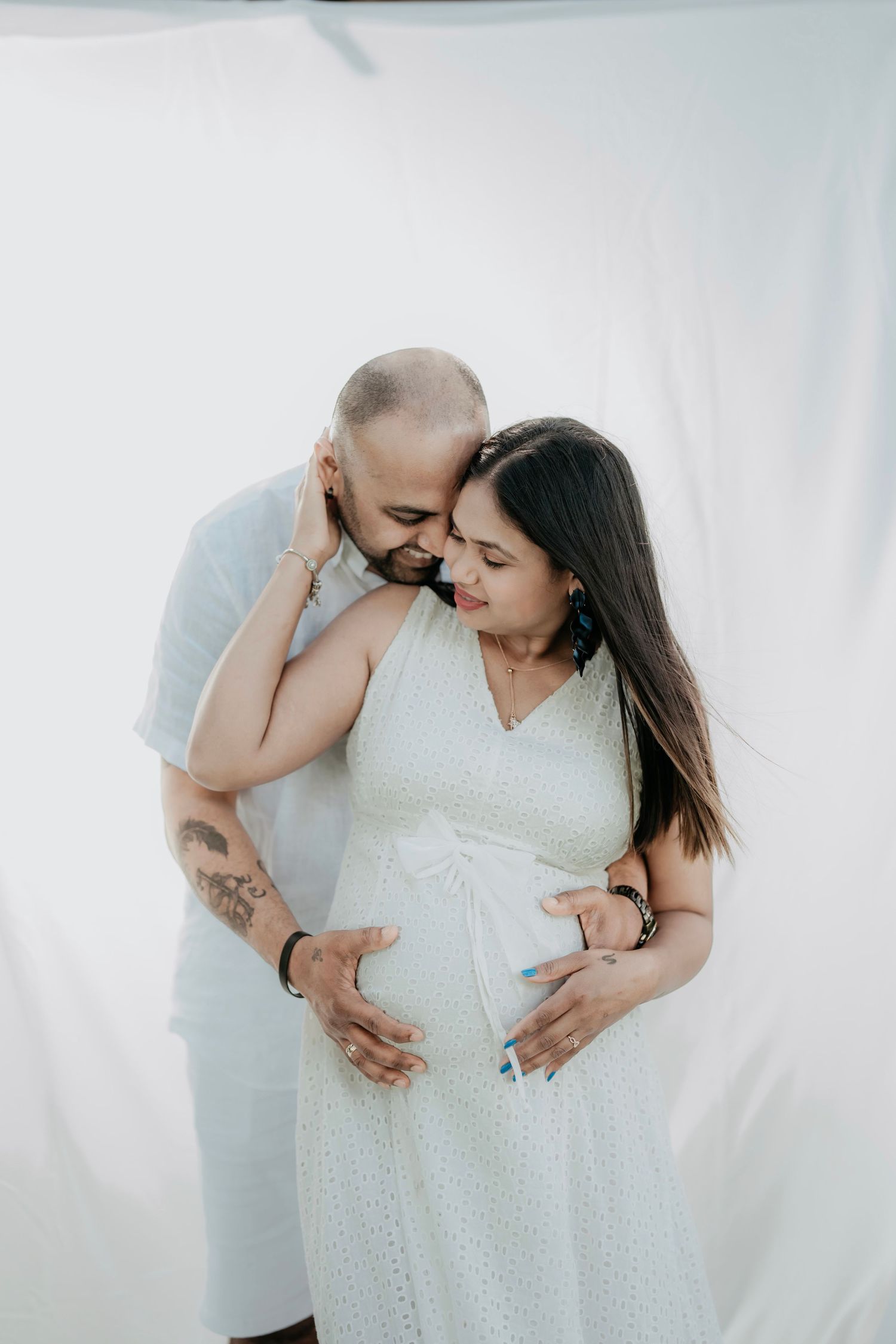 Intimate maternity photo of couple in white against light background.