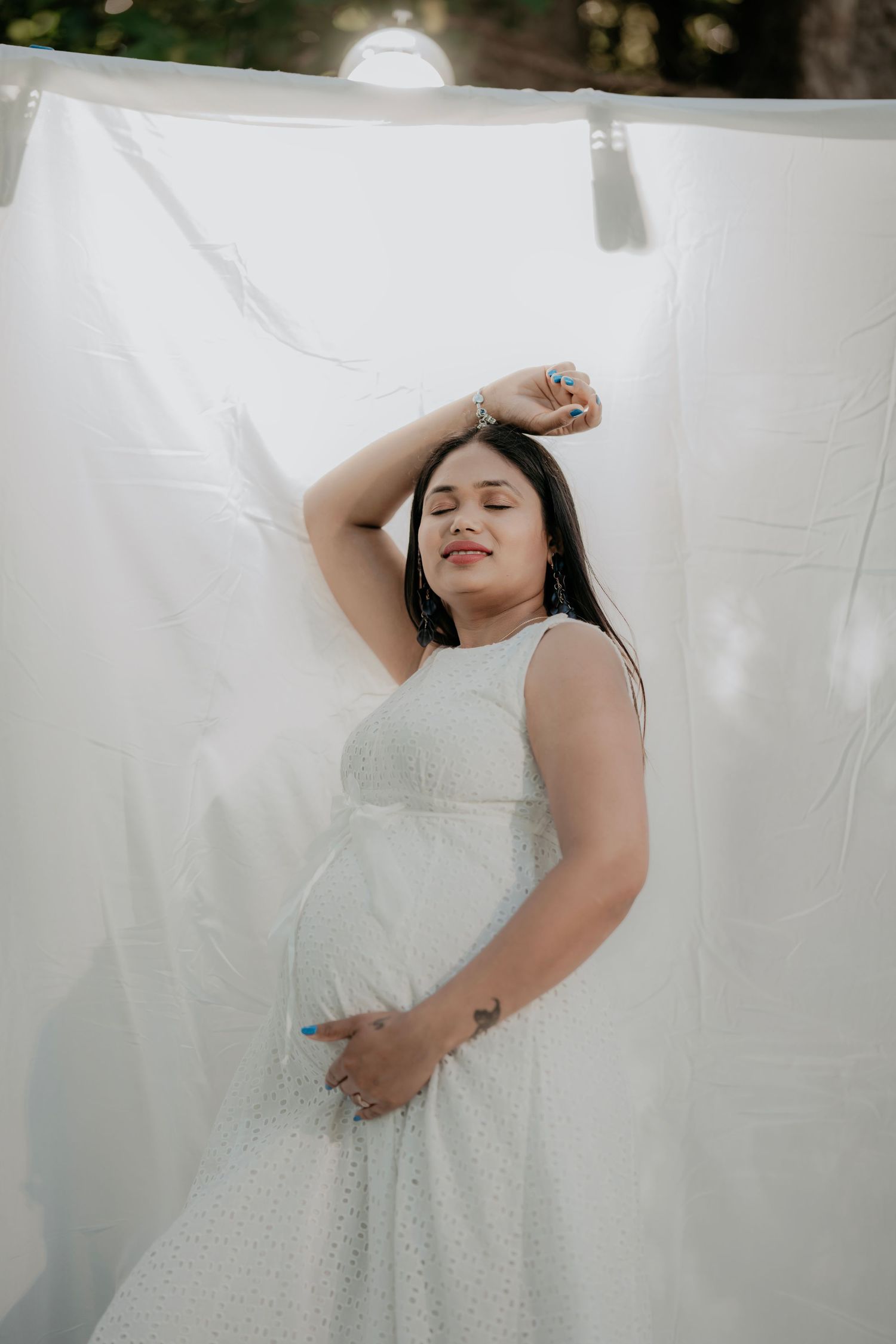 Artistic maternity portrait with white dress against draped fabric backdrop.