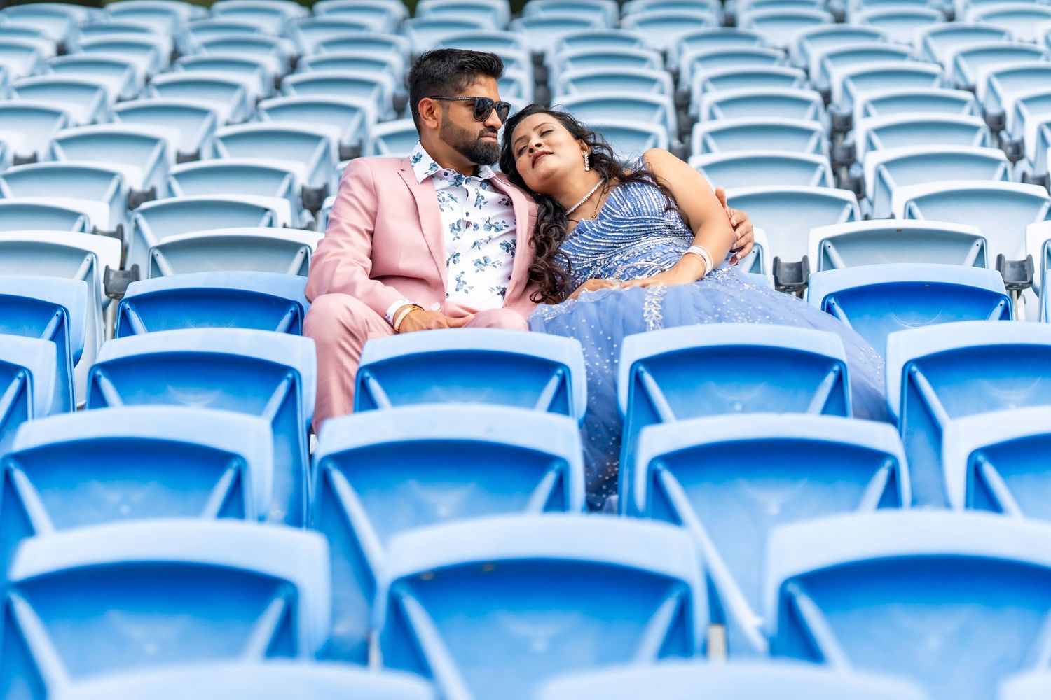 Couple sharing intimate moment while sitting in empty blue stadium seats.