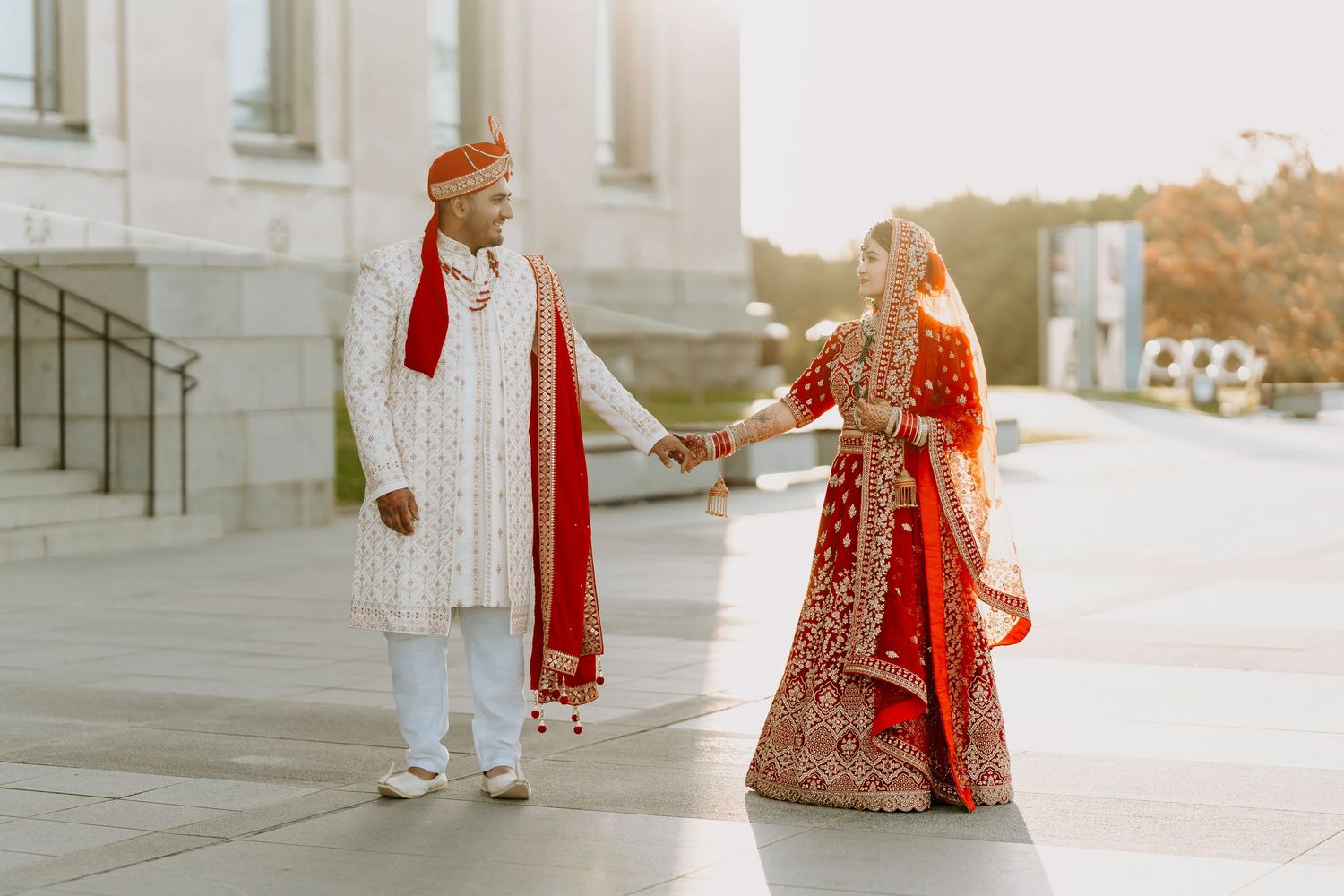 Traditional South Asian wedding couple holding hands outside a historic building.