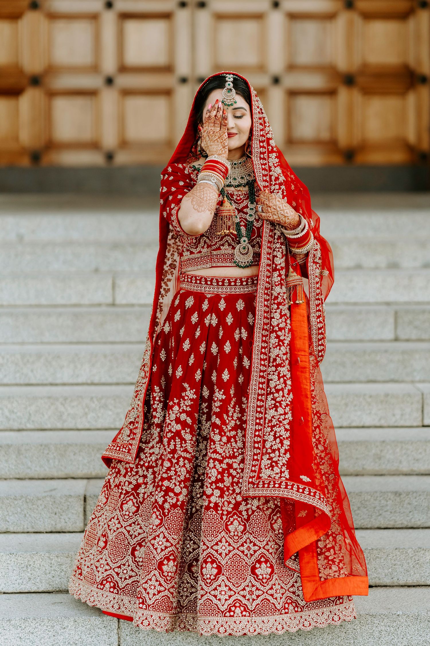Ornate red and gold Indian bridal lehenga with detailed embroidery work showcased on stone steps.