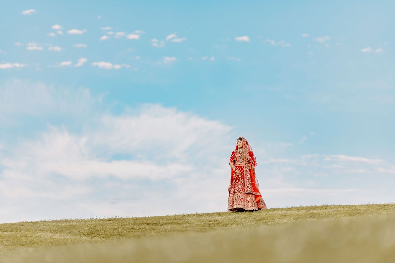 Traditional red dress silhouetted against blue sky and rolling hills in artistic outdoor portrait.