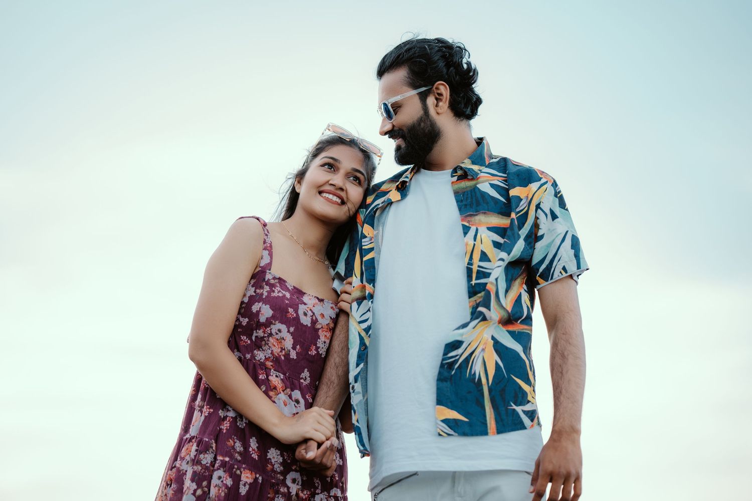 Romantic couple in summer outfits sharing a tender moment against blue sky.