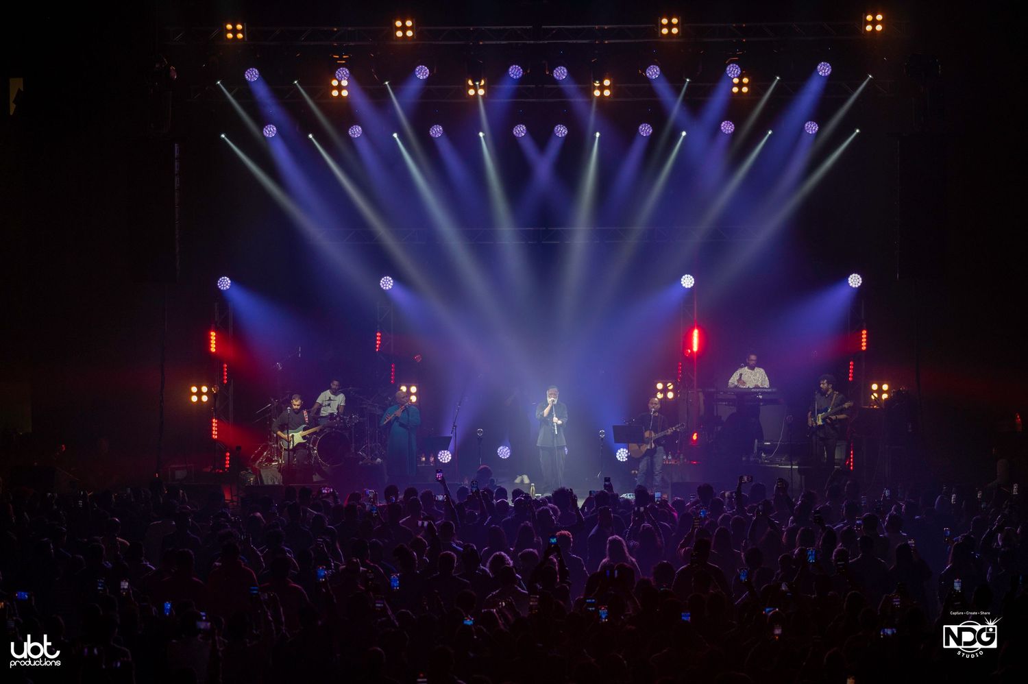 Energetic concert performance with blue stage lighting and crowd silhouette.
