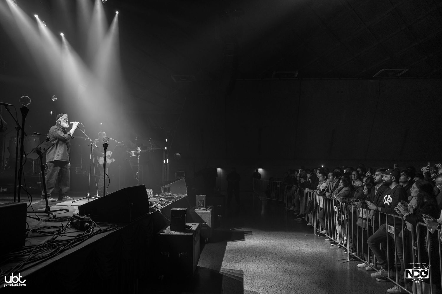 Concert venue with stage and crowd barrier shown in black and white.
