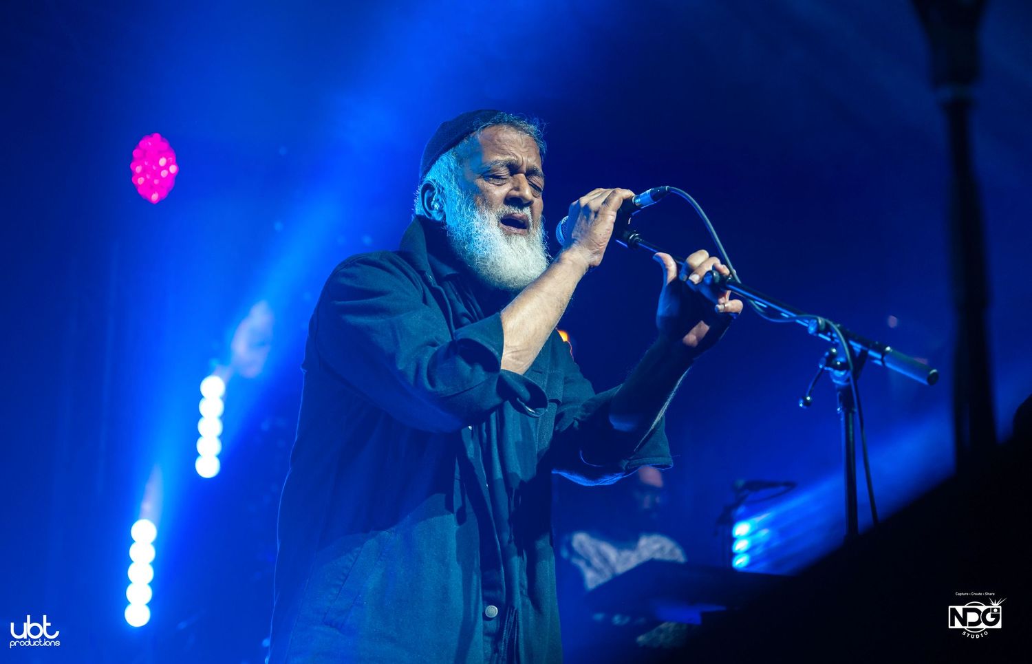 Concert performance with vivid blue lighting and musician against backlit stage.