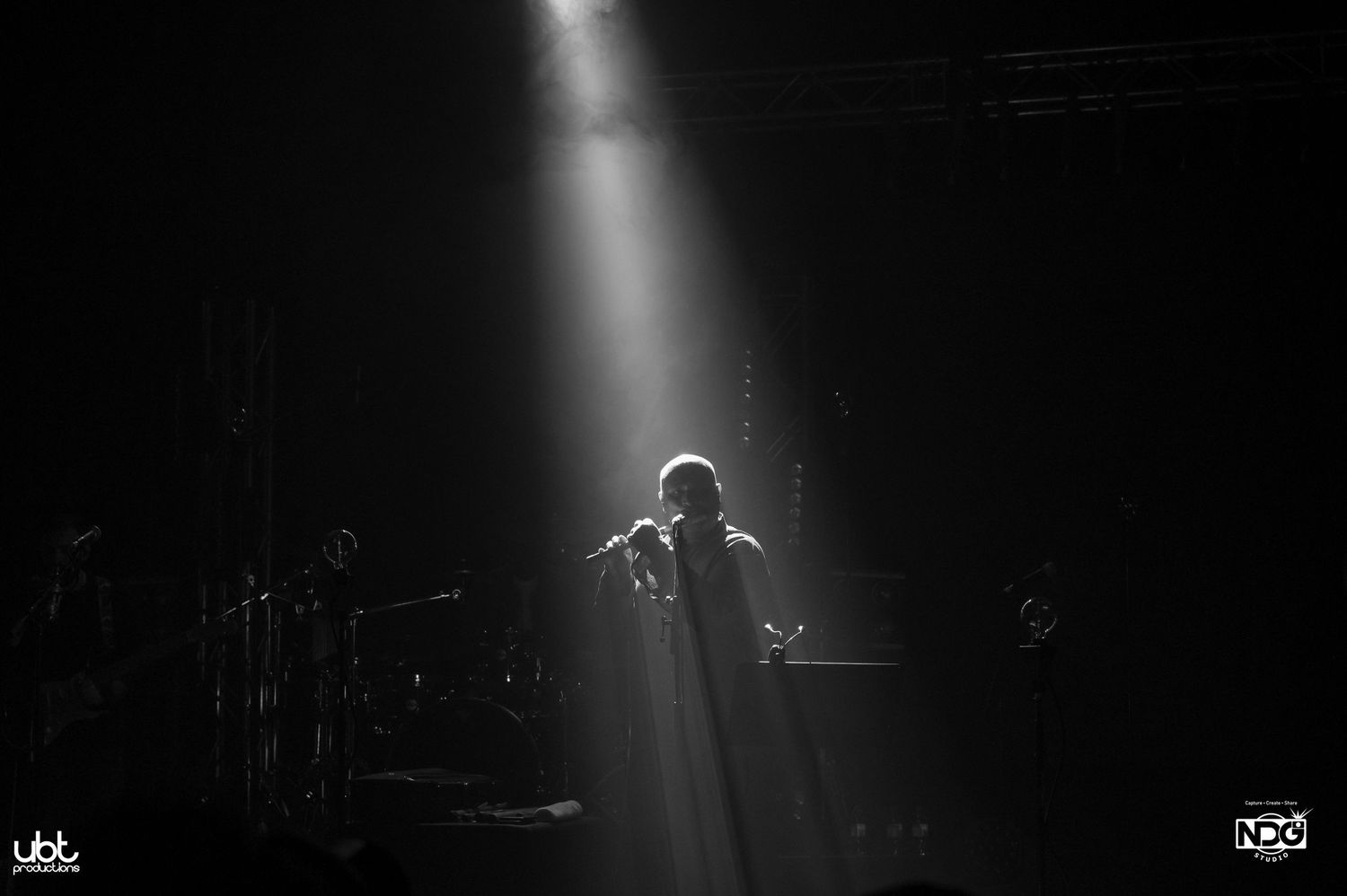 Dramatic spotlight illuminates a performer on dark stage.