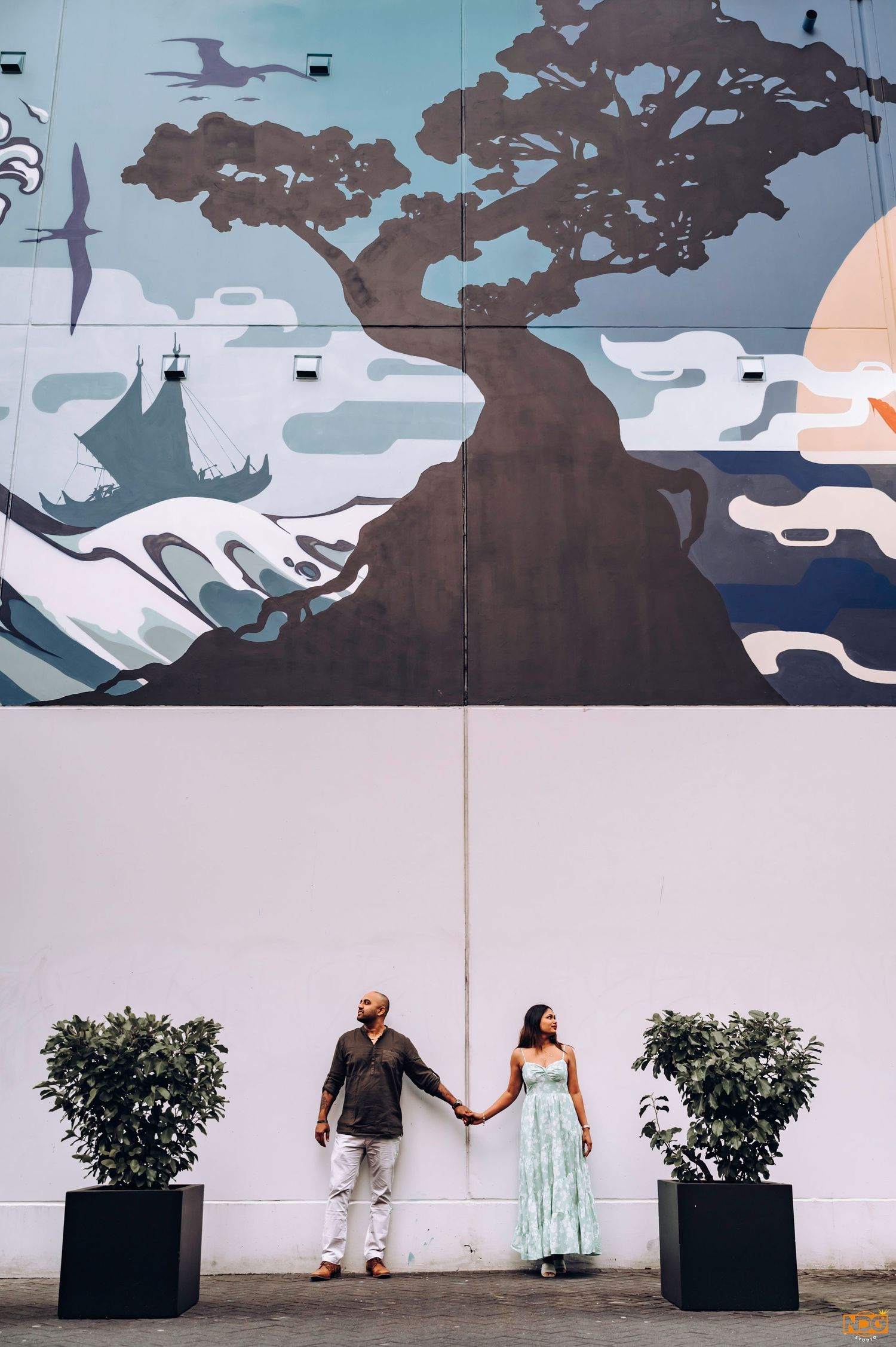Couple holding hands against artistic wall mural featuring trees and mountains.