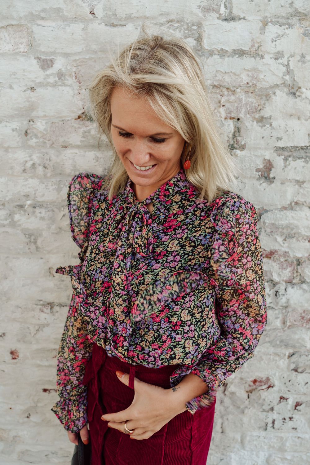 vrouw met bordeaux rokje en blouse met bloemetjes die het hoofd naar beneden houdt