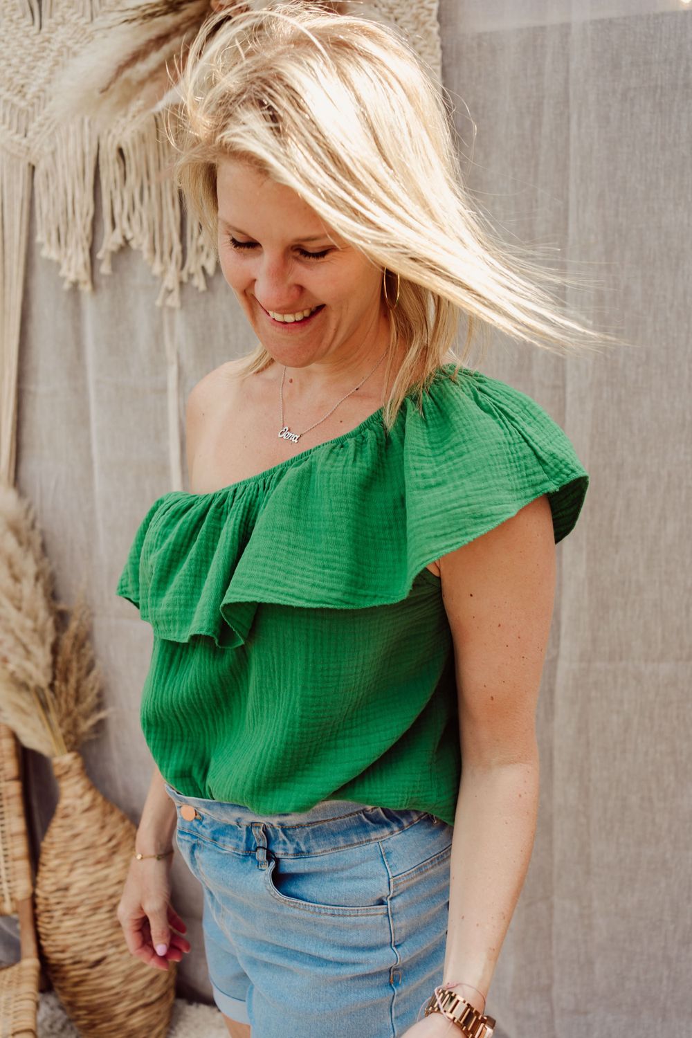 vrouw met jeansrok en groene blouse met slechts één schouder bedekt en boho achtergrond