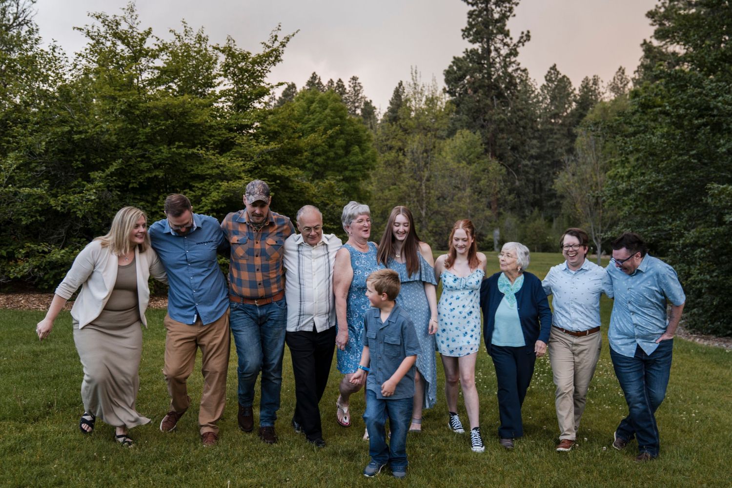 Family group photo outdoors with evergreen trees in background during golden hour.
