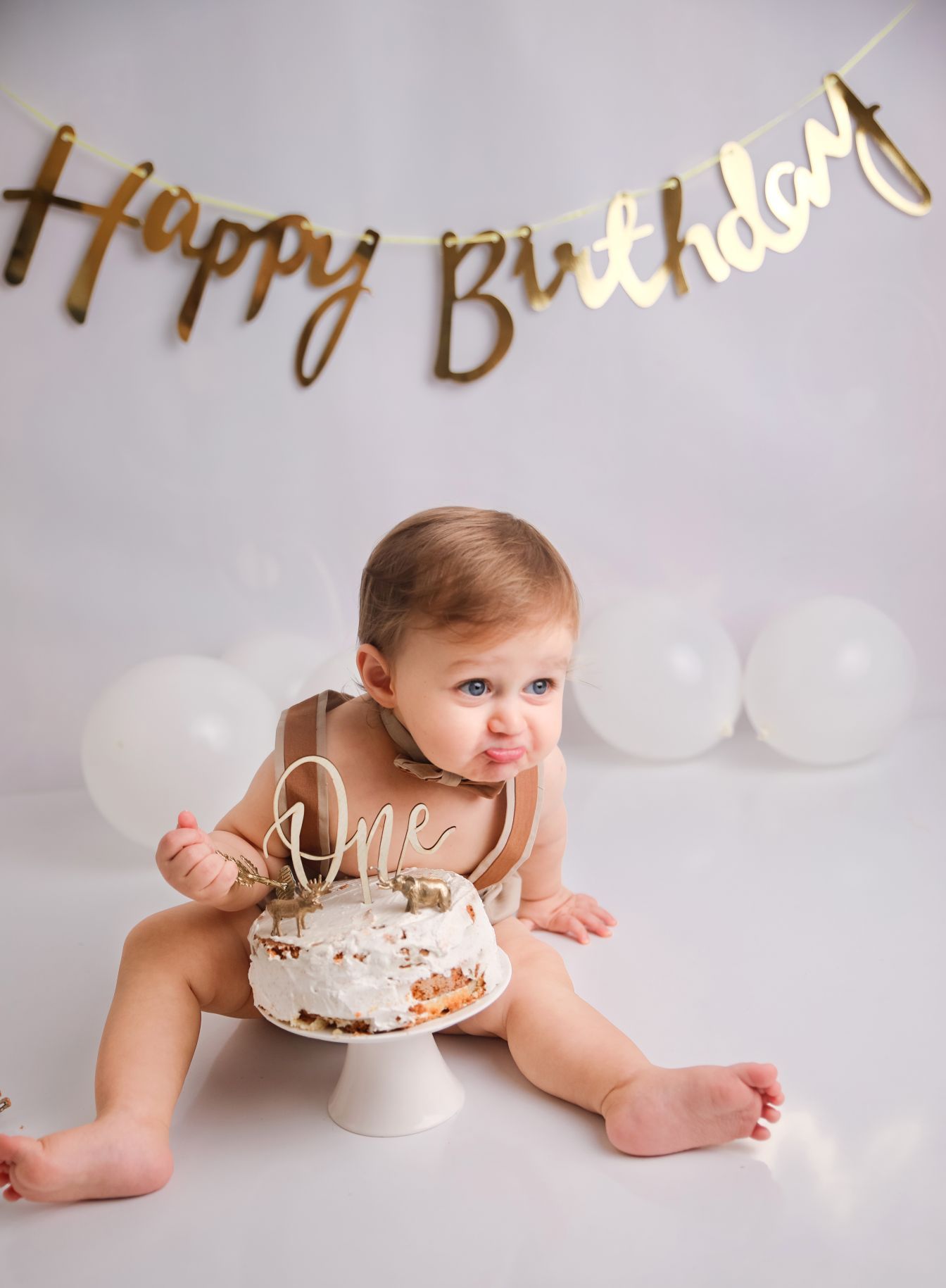 A baby's first birthday celebration with a cake and gold 'Happy Birthday' banner decoration.