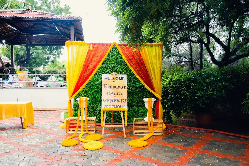 Colorful wedding mandap setup with orange and yellow drapes and chairs in an outdoor garden setting.