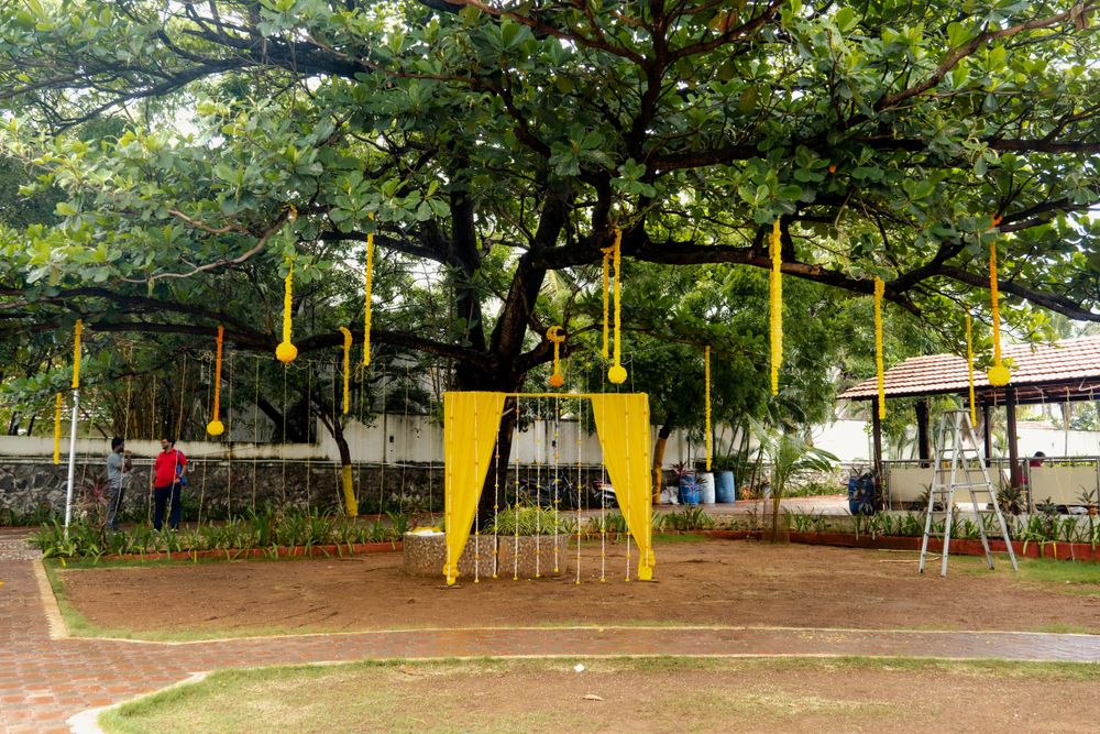 Outdoor event space with yellow poles and hanging decorations under large trees.