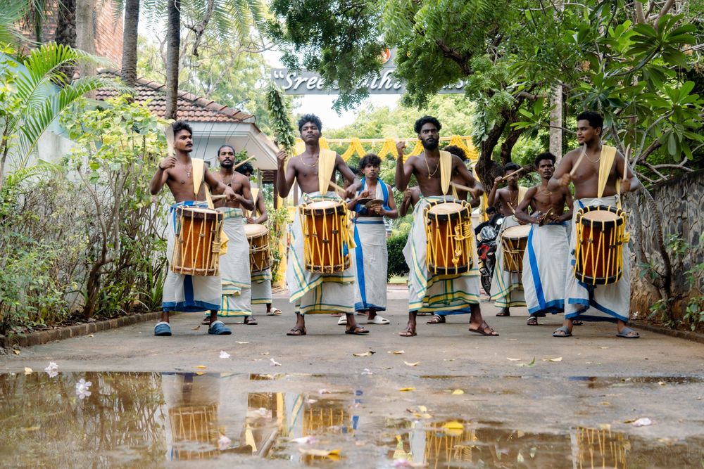 Musicians performing with traditional drums in a line with puddle reflection in foreground.