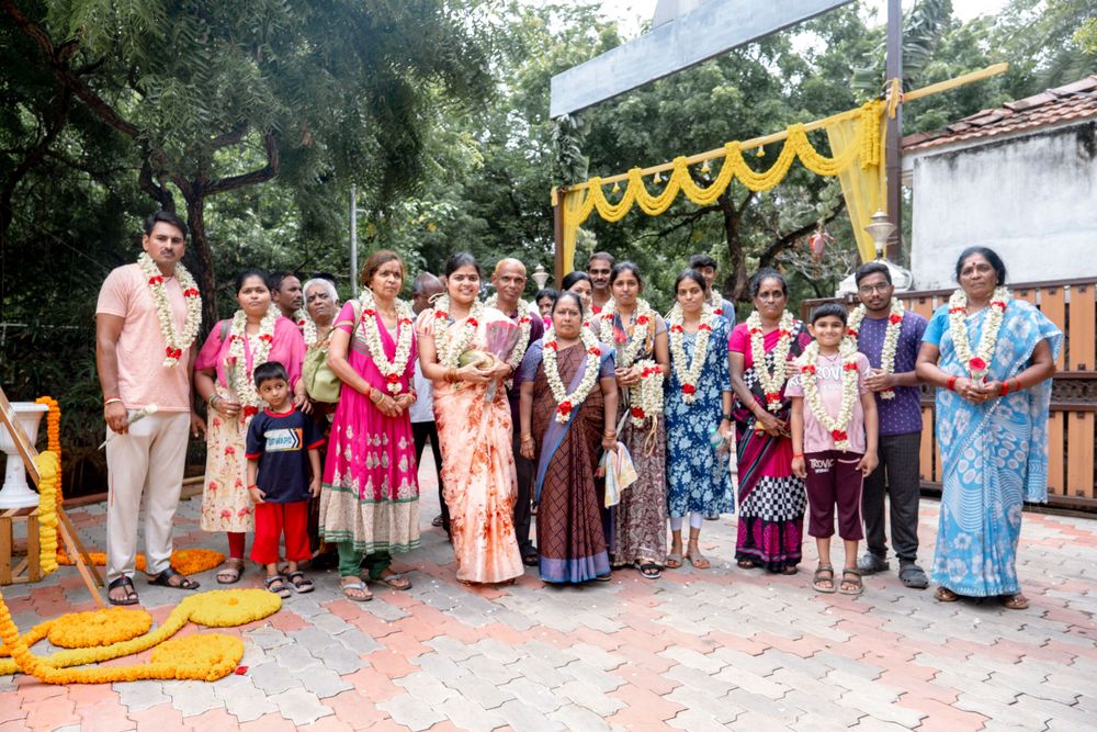 A group wearing colorful traditional Indian attire gathers at an outdoor event decorated with yellow floral garlands.