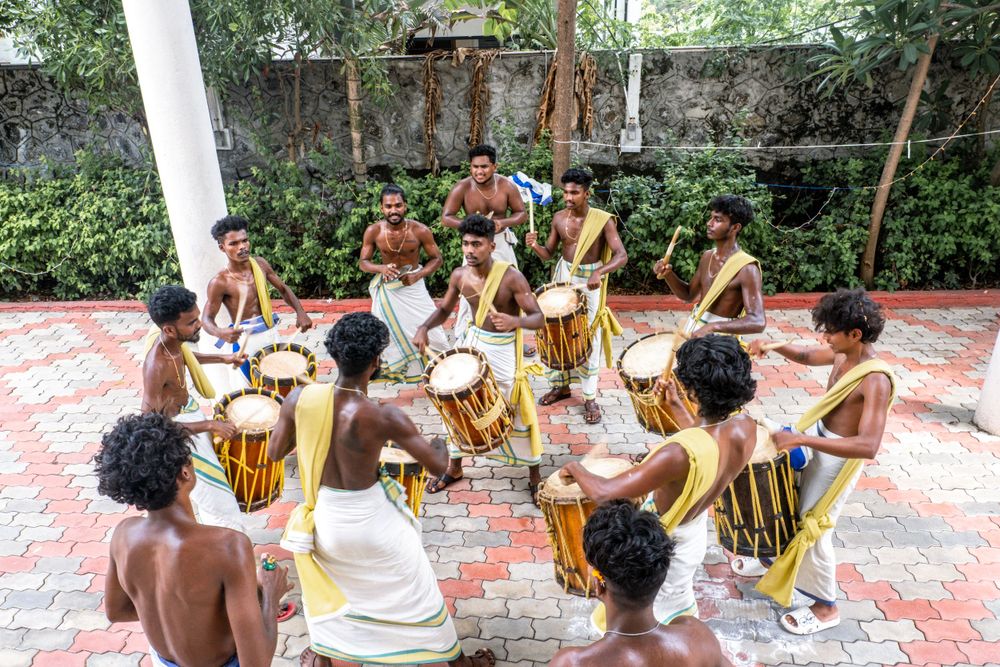 Performers play traditional African drums while seated in a circle on a tiled patio.