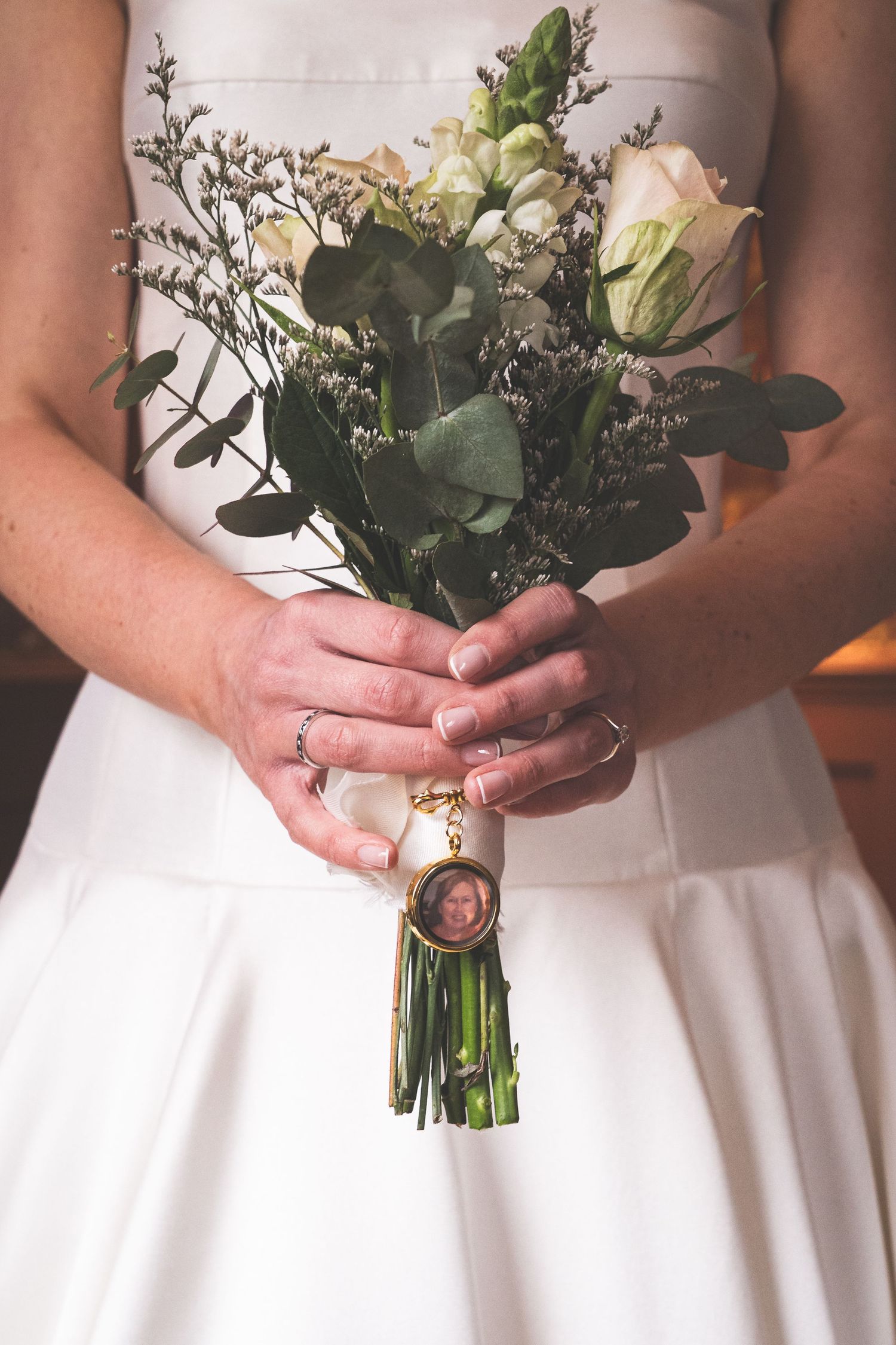 Close-up view of hands holding a delicate white and green wedding bouquet against a white dress.