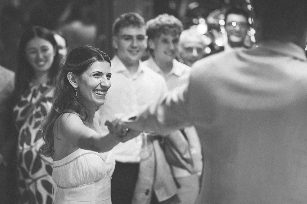 Black and white photo of a smiling bride in a white dress holding hands with groom at a wedding reception.