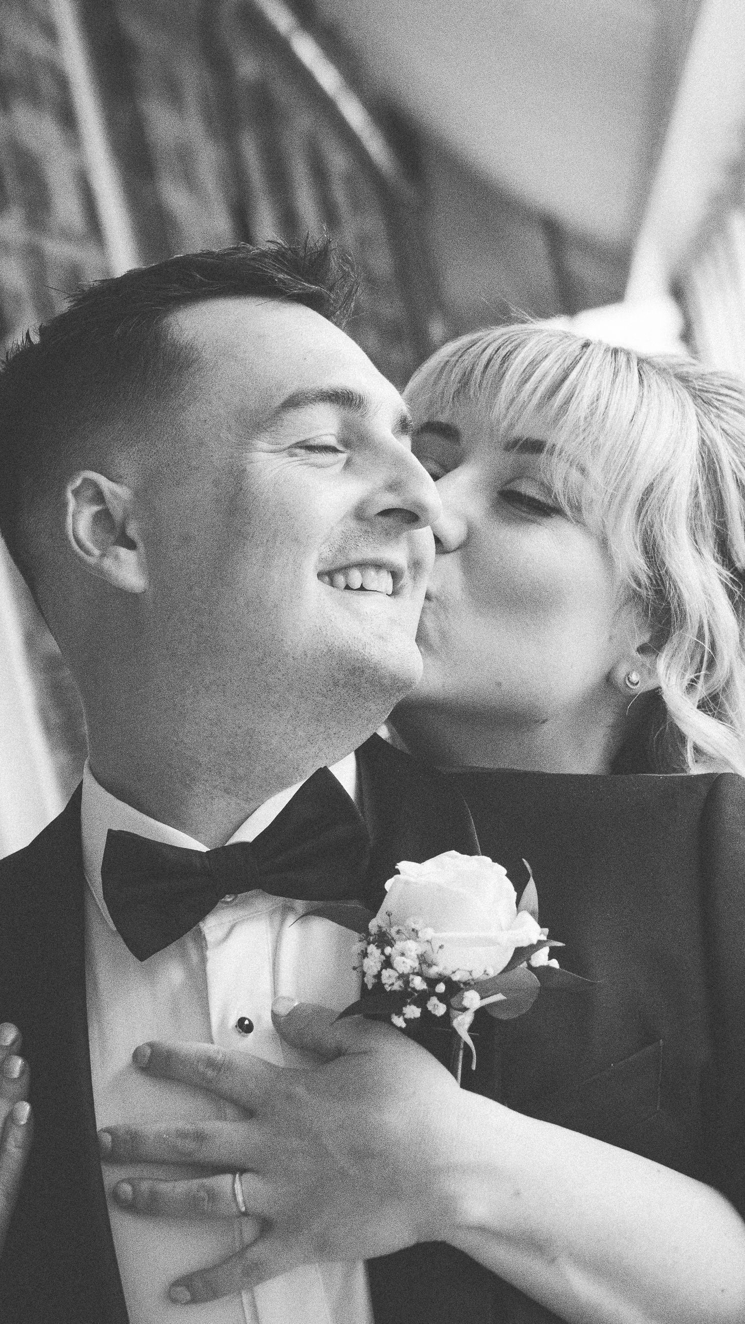 A romantic black and white wedding photo showing an intimate moment between a couple, with white rose boutonniere detail.