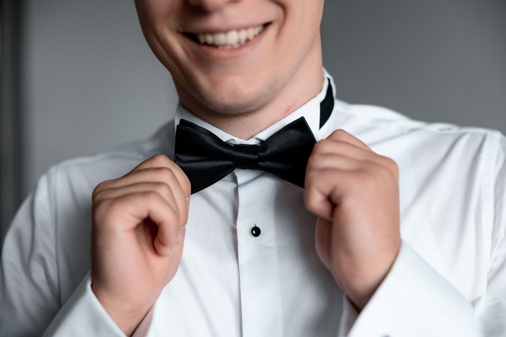 A close-up view of hands adjusting a black bowtie on a crisp white tuxedo shirt.