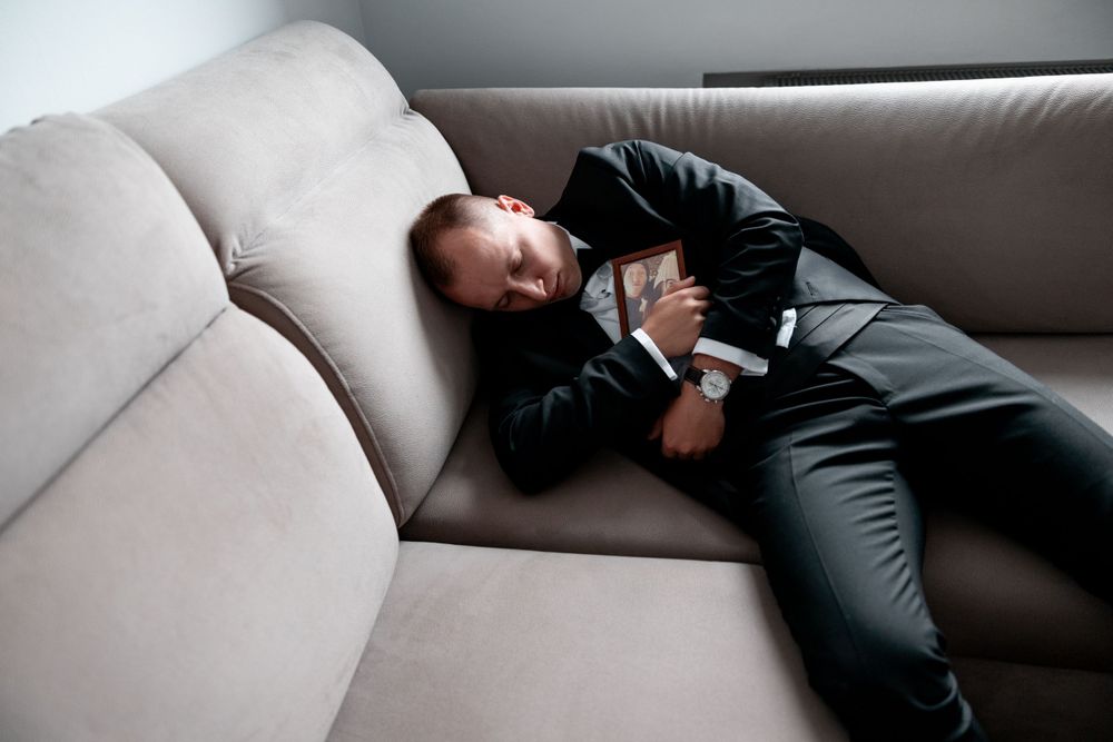 Person in formal attire resting on a beige couch during wedding preparations.