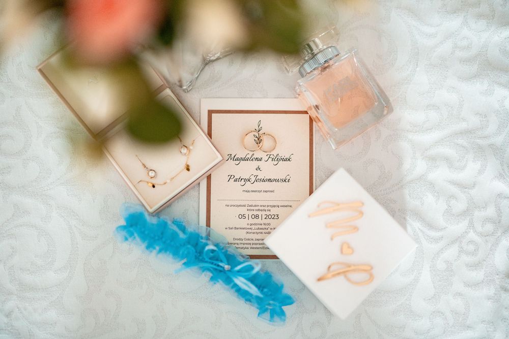 Wedding invitation and blue garter displayed on white lace fabric.