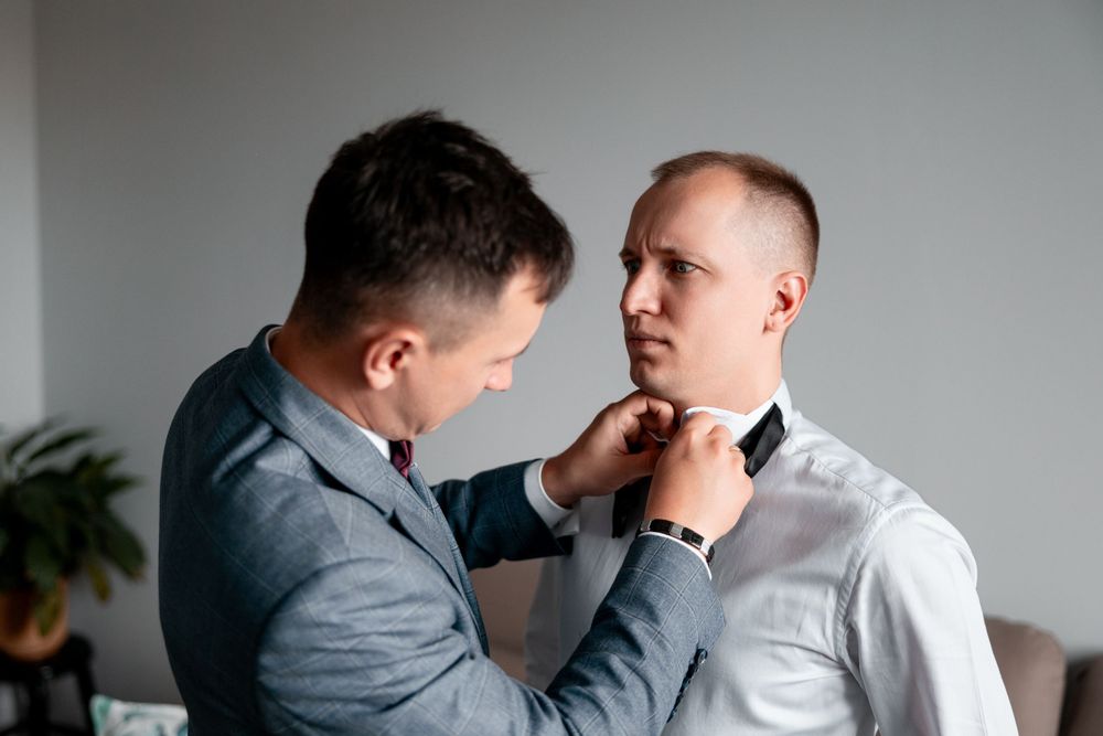 Close-up of hands adjusting black bow tie on white formal shirt.