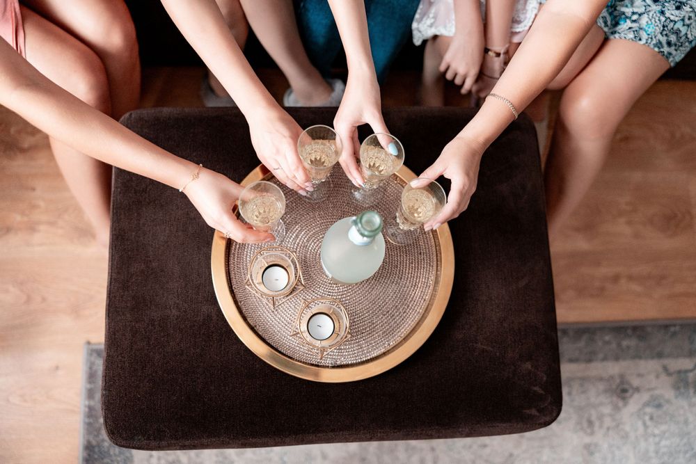 Multiple hands reach for shot glasses arranged on a round wooden tray.
