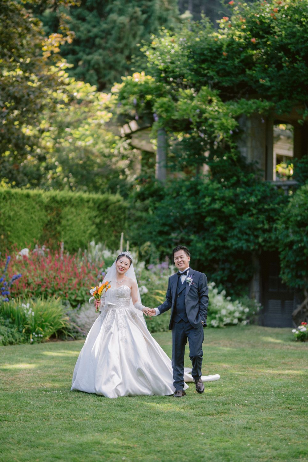 A couple celebrates their wedding day on a manicured lawn surrounded by colorful garden flowers.